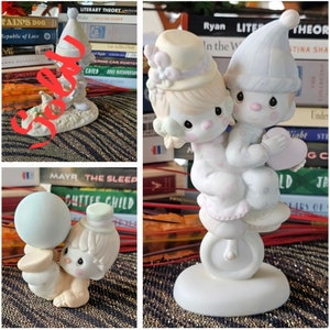 Könnte beinhalten: Eine Porzellanfigur, die zwei Kinder im Schlafanzug auf einem Einrad zeigt. Ein Kind trägt eine Schlafmütze und hält ein Herz, das andere einen Hut mit Blumen. Die Figuren haben helle Haut, rosige Wangen und große dunkle Augen in sanften Pastelltönen wie Blau, Rosa und Creme.