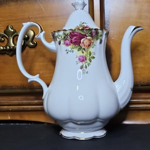 以下が含まれることがあります： 赤、黄、ピンクのバラの花柄が描かれた、金色の縁取りのある白い磁器製のティーポット。ティーポットには蓋と取っ手があります。