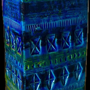 May include: A blue ceramic vase with a geometric pattern. The vase is square shaped and decorated with a repeating design of diamonds and lines.