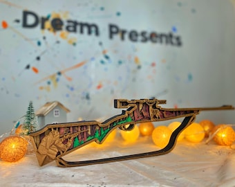 May include: A wooden cutout of a sniper rifle with a camouflage design. The rifle is intricately detailed and features a soldier aiming with a scope. The cutout is displayed on a table with a string of lights in the background.