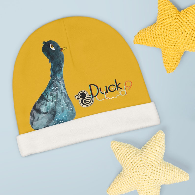 Puede incluir: Un gorro amarillo con un borde blanco presenta una ilustraci&oacute;n de pato azul y gris y el texto "Duck Cloud" en letras de colores.