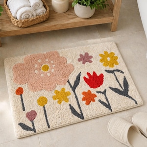 May include: A rectangular bath mat with a cream background and a floral design. The flowers are in shades of pink, yellow, red, and orange, with gray stems and leaves. The mat is made of a soft, textured material.
