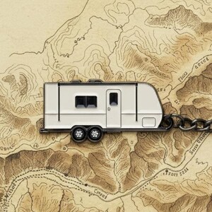 May include: A white travel trailer keychain with black wheels and a black key ring. The keychain is connected by a chain and is set against a detailed map background, evoking a sense of adventure and travel.