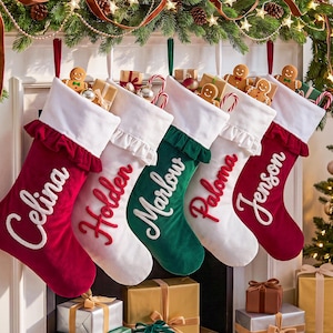 Könnte beinhalten: Fünf Weihnachtsstrümpfe mit weißen Stulpen und Rüschenbesatz, bestickt mit den Namen Celina, Holden, Marlow, Paloma und Jenson. Die Strümpfe aus rotem, weißem und grünem Samt enthalten kleine Geschenkboxen und Lebkuchenmänner.