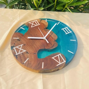 May include: Round wooden clock with a turquoise resin center and natural wood grain. The clock face features white Roman numerals and hands. The clock is approximately 10 inches in diameter.