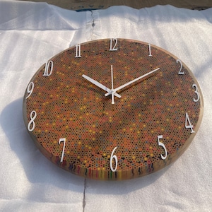 May include: A round clock with white numbers and hands. The clock face is made of a mosaic of colored pencil shavings.