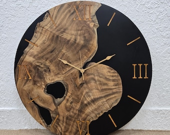May include: A round wooden clock with black epoxy resin. The clock face has Roman numerals and gold-colored hands.