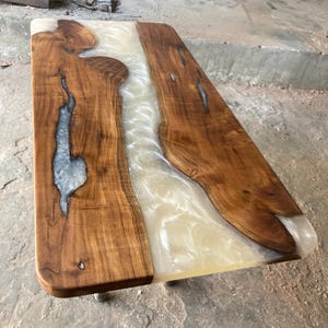 Könnte beinhalten: Ein Holz-Couchtisch mit einem weißen Harzfluss, der durch die Mitte fließt. Der Tisch hat eine natürliche Holzoptik und wird von Metallbeinen getragen.