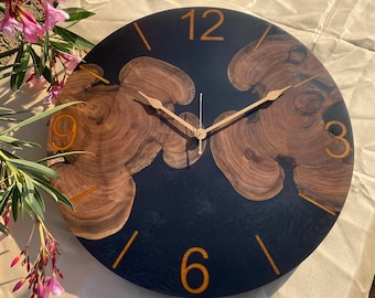 May include: A round wooden clock with black resin and gold accents. The clock face has Roman numeral markings and gold hands.