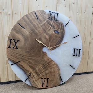 May include: A round wooden and white resin wall clock with Roman numeral markings. The clock has gold hands and a black background for the numbers.