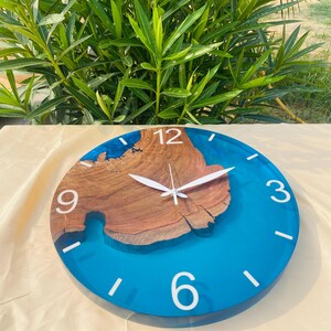 May include: A round wall clock with a wooden center and a vibrant blue resin border. White numerals mark the hours, and the clock hands are white. The clock's diameter is approximately 12 inches.