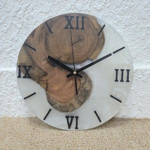May include: A white and brown resin clock with Roman numeral markings. The clock face is a combination of white resin and a wood slice.