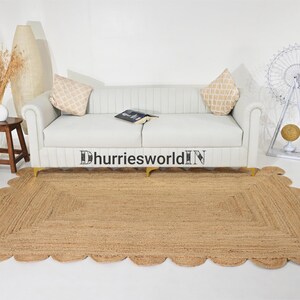 May include: A light brown jute rug with a scalloped edge. The rug is placed in front of a white sofa with two pillows. The rug is approximately 5 feet long and 3 feet wide.