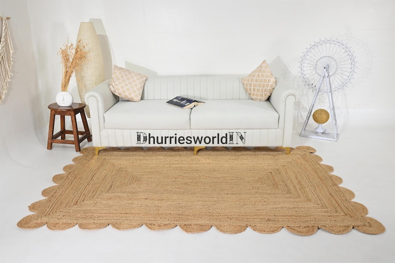 May include: A light brown jute rug with a scalloped edge. The rug is placed in front of a white sofa with two pillows. The rug is approximately 5 feet long and 3 feet wide.