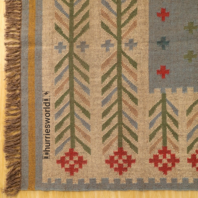 May include: Close-up of a woven rug with a beige background and a repeating pattern of green, blue, and red geometric shapes. The rug has a fringed edge and the text "dhurriesworld" is visible on the side.