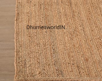 May include: A close-up of a natural fiber rug with a woven texture. The rug is a light brown color and has a slightly rough surface. The text "DhurriesworldIN" is visible in the center of the rug.