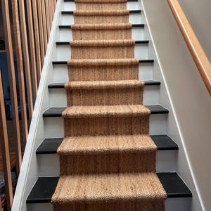 May include: A set of stairs with black painted risers and white painted treads. A natural fibre rug runner covers the stairs.