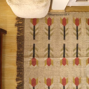 May include: Beige rug with a repeating pattern of red and yellow tulip-like flowers on black stems. The rug has a fringed edge and the text "hurriesworld!" is visible in the top right corner.