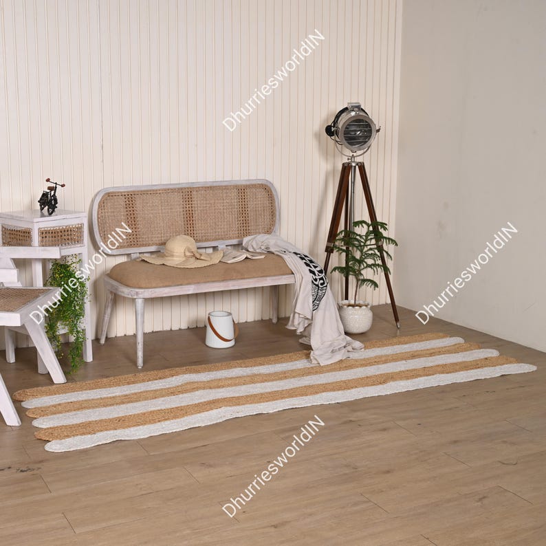 May include: A white woven bench with a jute cushion and a white and brown striped jute rug. A potted plant and a vintage style floor lamp are in the background.