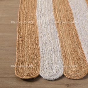 May include: A jute rug with alternating stripes of natural beige and white. The rug has a woven texture and a rounded shape.