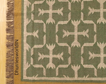 May include: A green and beige patterned rug with a geometric design. The rug has a gold border and a fringe on one side. The text "DhurriesworldIN" is printed vertically on the left side of the rug.