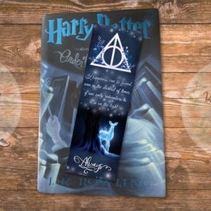 May include: A Harry Potter book with a bookmark featuring the Deathly Hallows symbol and a glowing Patronus. The bookmark has the quote, "Happiness can be found, even in the darkest of times, if one only remembers to turn on the light."