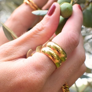 Könnte beinhalten: Nahaufnahme einer Hand, die zwei goldene Ringe trägt. Die Ringe sind übereinander gestapelt und haben ein abgerundetes, glattes Design.