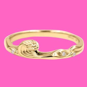 Könnte beinhalten: Ein goldener Wellenring mit drei kleinen Diamanten. Die Welle ist stilisiert und hat eine strukturierte Oberfläche.