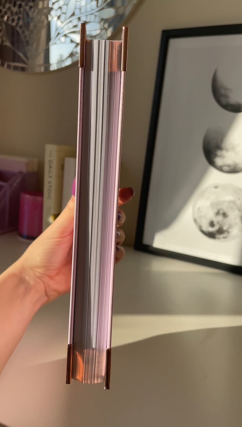 May include: A close-up of the spine of a book with a light purple cover and gold accents. The book is closed and the pages are visible.