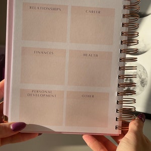 May include: A pink and white spiral bound notebook with a section for long-term goals. The sections are labeled: Relationships, Career, Finances, Health, Personal Development, and Other.