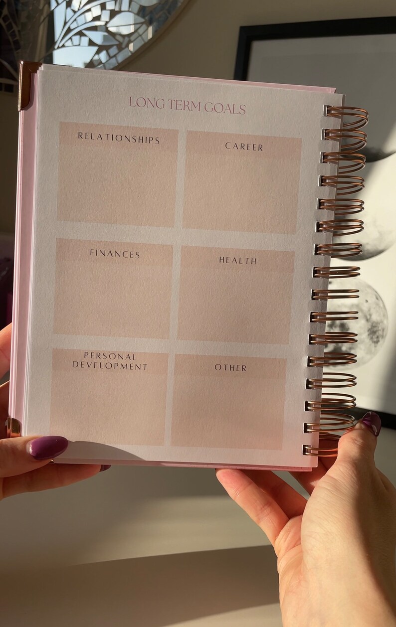 May include: A pink and white spiral bound notebook with a section for long-term goals. The sections are labeled: Relationships, Career, Finances, Health, Personal Development, and Other.