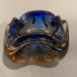 Puede incluir: Un cenicero de vidrio marrón y azul con una forma ondulada y orgánica.