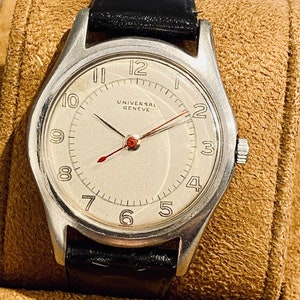 May include: A silver wristwatch with a white face and black leather strap. The watch face has black Roman numeral hour markers and a red second hand. The watch face also has the text "UNIVERSAL GENEVE" printed on it.