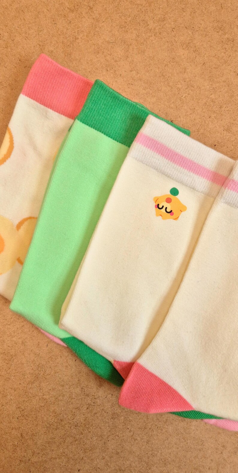 K&ouml;nnte beinhalten: Vier Paar bunte Socken. Ein Paar hat einen rosa Bund und Ferse, ein anderes einen gr&uuml;nen Bund und ein drittes ein Cupcake-Motiv. Die Socken sind cremefarben, gr&uuml;n und rosa.