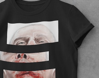 May include: Black t-shirt featuring a graphic print of a man's face in three sections. The top section shows the forehead and eyes, the middle section shows the nose, and the bottom section shows the mouth and chin. The mouth is covered in red paint.
