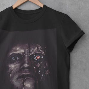 May include: Black t-shirt with a graphic print of a face that is half human and half robot. The robot side has a red eye.
