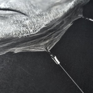 May include: A close-up of a man's face drawn in black and white charcoal. The drawing is very detailed and realistic. The man has a beard and is looking down.