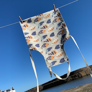 Puede incluir: Un delantal azul y naranja con un patrón de peces colgando de una cuerda para tender la ropa contra un cielo azul brillante.