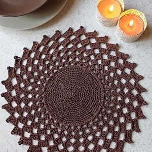 May include: A brown crocheted doily with a circular design. The doily is made with a delicate, lacy pattern and has a smooth, even texture.