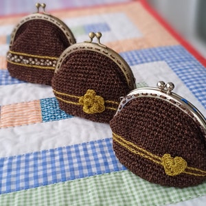 May include: Three brown crocheted coin purses with gold trim and metal clasps. The purses are on a blue and white checkered fabric.