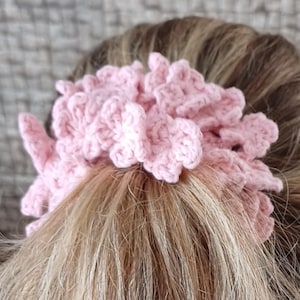 May include: A pink crocheted hair scrunchie with a ruffled design.