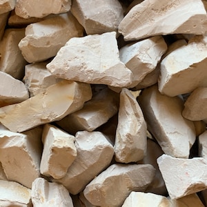 May include: A close-up of a pile of small, irregular, light grey rocks. The rocks are smooth and have a slightly rough texture.