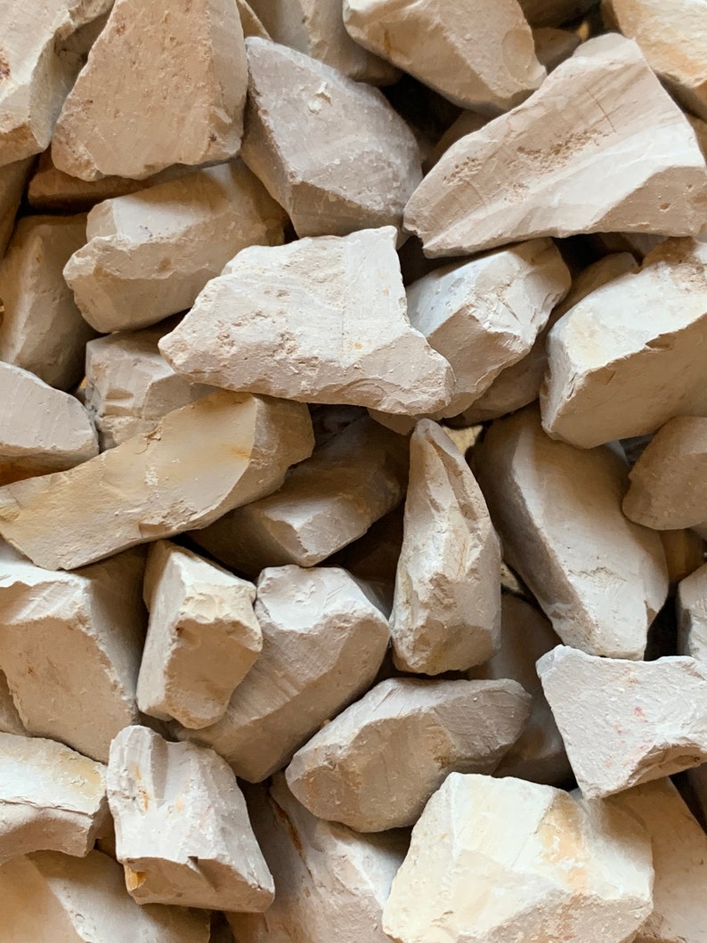 May include: A close-up of a pile of small, irregular, light grey rocks. The rocks are smooth and have a slightly rough texture.