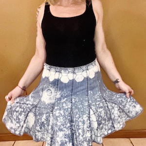 May include: A denim skirt with a white bleach design. The skirt has a honeycomb pattern and is pleated.