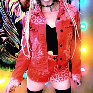 Puede incluir: Una chaqueta vaquera roja y unos pantalones cortos a juego con un estampado floral blanco. La chaqueta tiene cierre de botones y cuello. Los pantalones cortos tienen cintura y bolsillos.