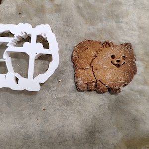 Könnte beinhalten: Ein weißer Plastik-Ausstecher in Form eines Hundes, neben einem braunen Lebkuchen in Form eines Hundes.