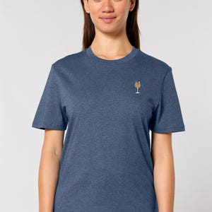 May include: A blue t-shirt with a small embroidered cocktail glass design on the chest. The shirt has short sleeves and a crew neck. The fabric appears to be a soft, heathered material.