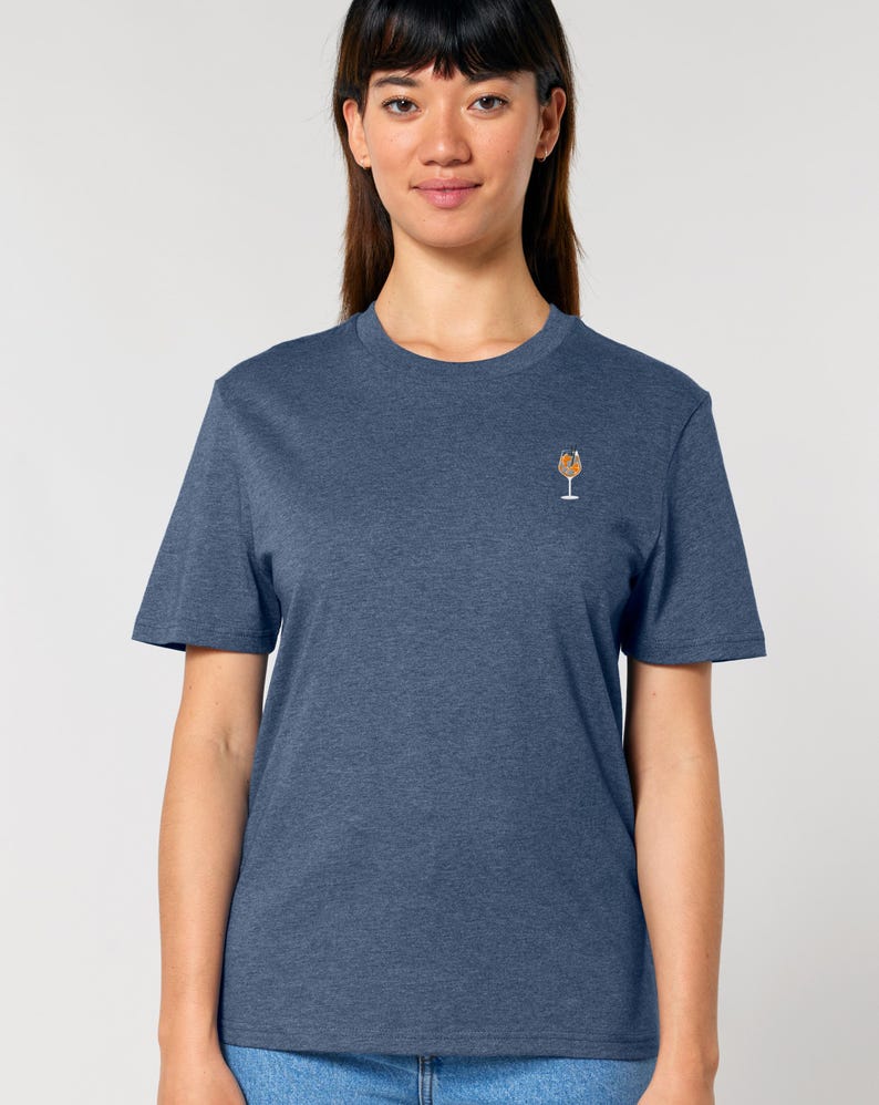 May include: A blue t-shirt with a small embroidered cocktail glass design on the chest. The shirt has short sleeves and a crew neck. The fabric appears to be a soft, heathered material.