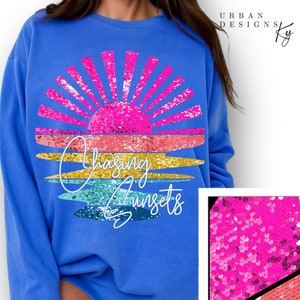 May include: A royal blue sweatshirt with a glittery pink, orange, yellow, and blue sunset graphic and the text "Chasing Sunsets".