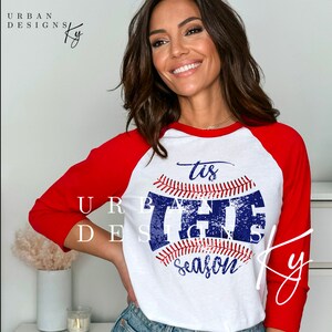 May include: A white and red baseball raglan t-shirt with a blue and white baseball graphic that says "'tis the season".